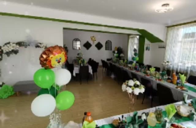Sala restaurantului pregătită pentru o petrecere: mese lungi cu fețe de masă albe și verzi, baloane